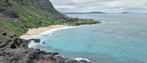 A coastal landscape with a beach, rocky cliffs, and a view of the ocean.