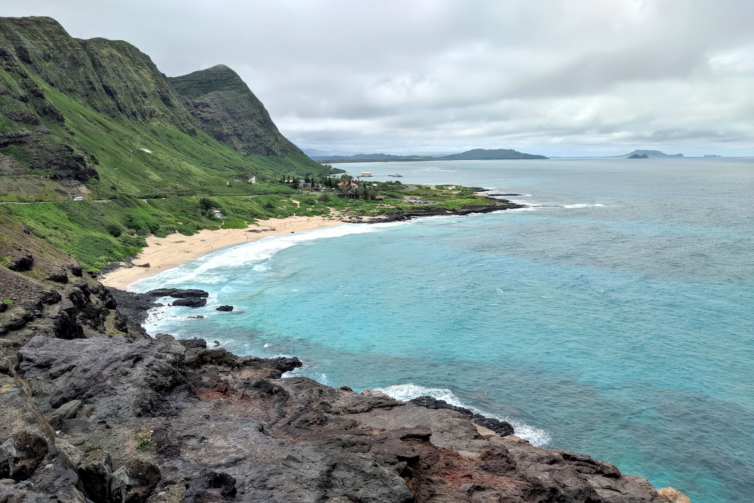 Un paysage côtier avec une plage, une côte rocheuse et une montagne en arrière-plan.