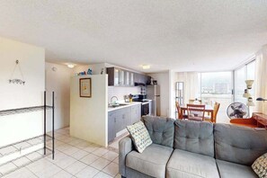 A compact living space with a kitchenette, a sofa, a dining table, and a view through large windows. - Waikiki High Rise - 30 night minimum (Honolulu)
