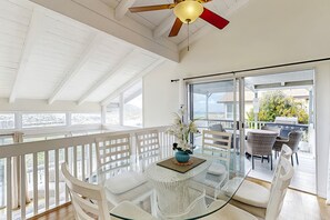 Un balcon spacieux avec une table en verre, des chaises blanches et un ventilateur de plafond.