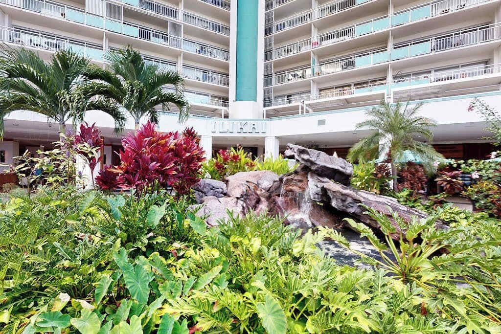 A hotel with multiple balconies, a central water feature, and lush tropical landscaping.