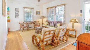 Una habitación con ventilador de techo, muebles de mimbre, una mesa de madera y dos ventanas con persianas.