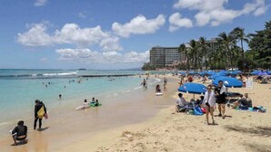 Uma praia com pessoas, guarda-sóis e um edifício ao fundo.