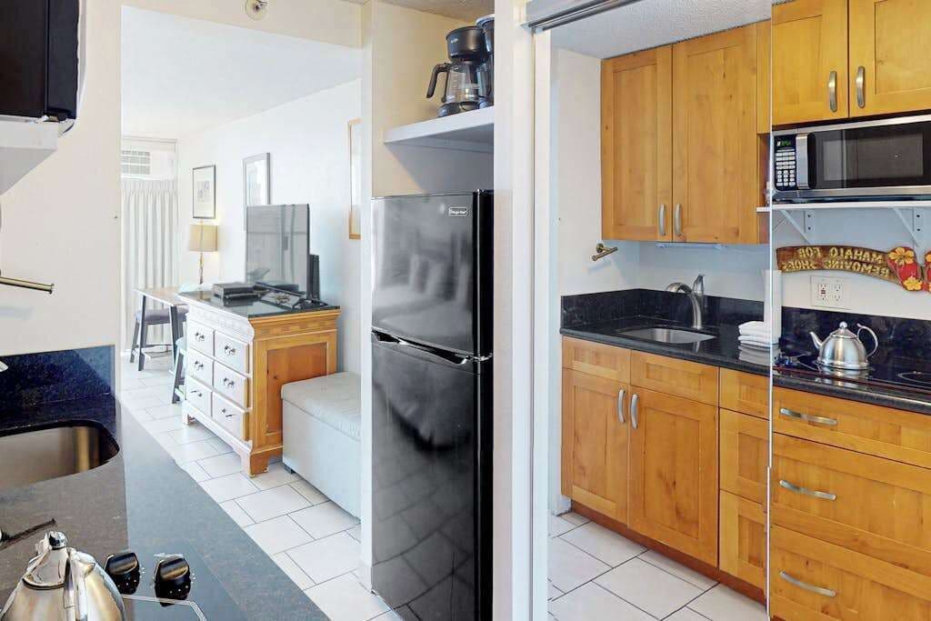 A compact kitchen with wooden cabinets, a stainless steel refrigerator, a microwave, and a sink.