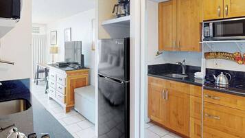A compact kitchen with wooden cabinets, a stainless steel refrigerator, a microwave, and a sink.