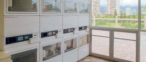 Un cuarto de lavandería con varias lavadoras, piso de baldosas de piedra y vista a un paisaje urbano a través de un ventanal grande.