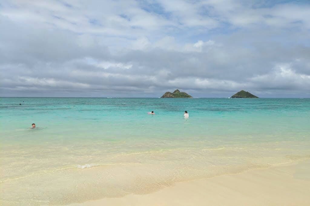 A beach with clear turquoise water, sandy shore, and two small islands in the distance.