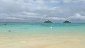 A beach with clear turquoise water, sandy shore, and two small islands in the distance.