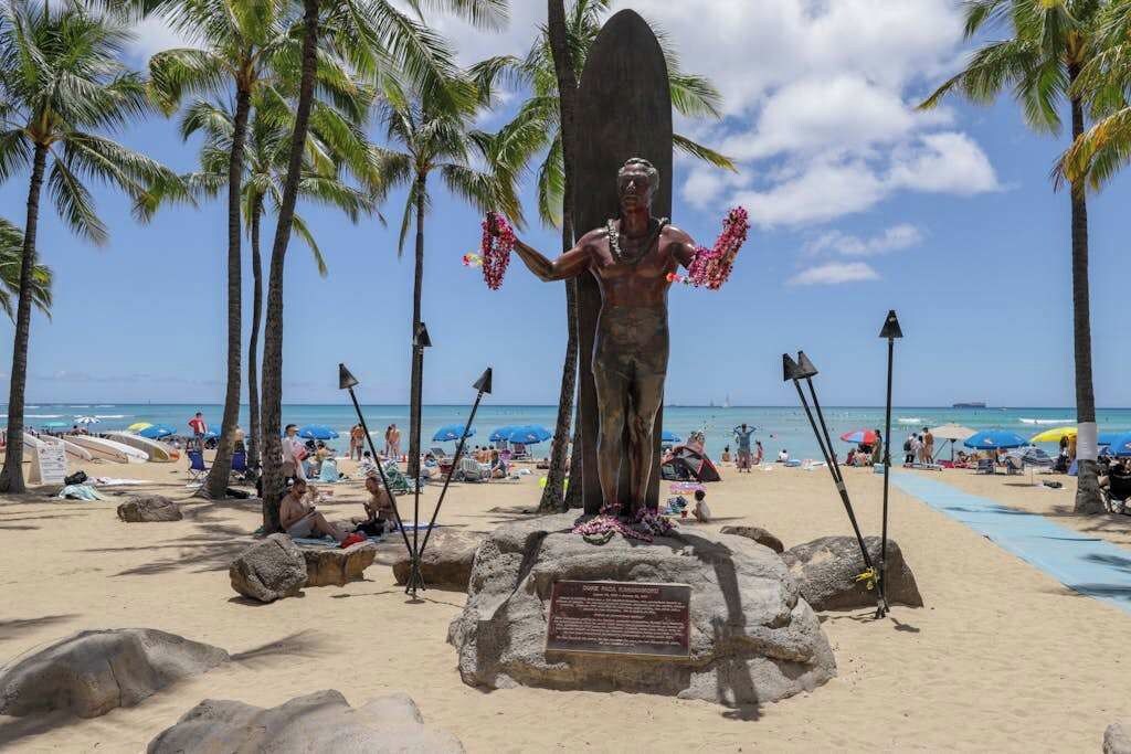 A beach with a statue, palm trees, and a clear sky.