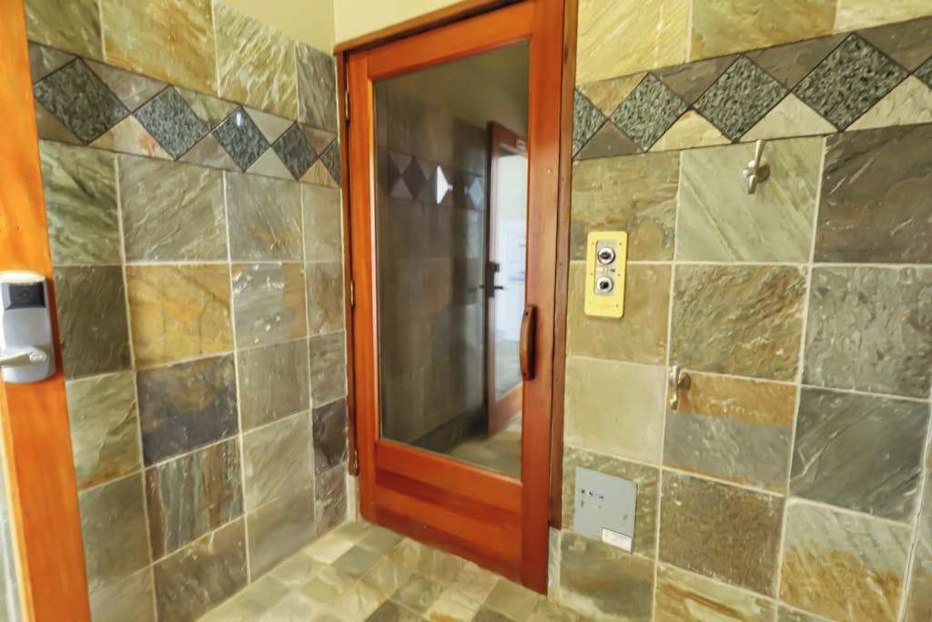 Une salle de bain avec une porte en bois, des murs carrelés et une prise électrique visible.
