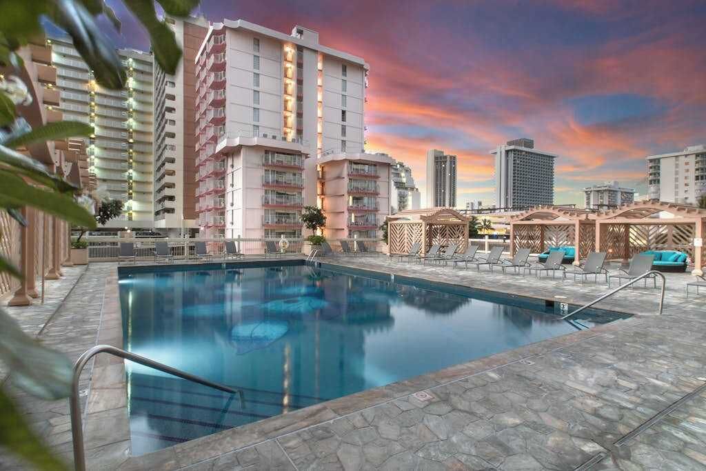 A swimming pool with lounge chairs and umbrellas, surrounded by high-rise buildings.