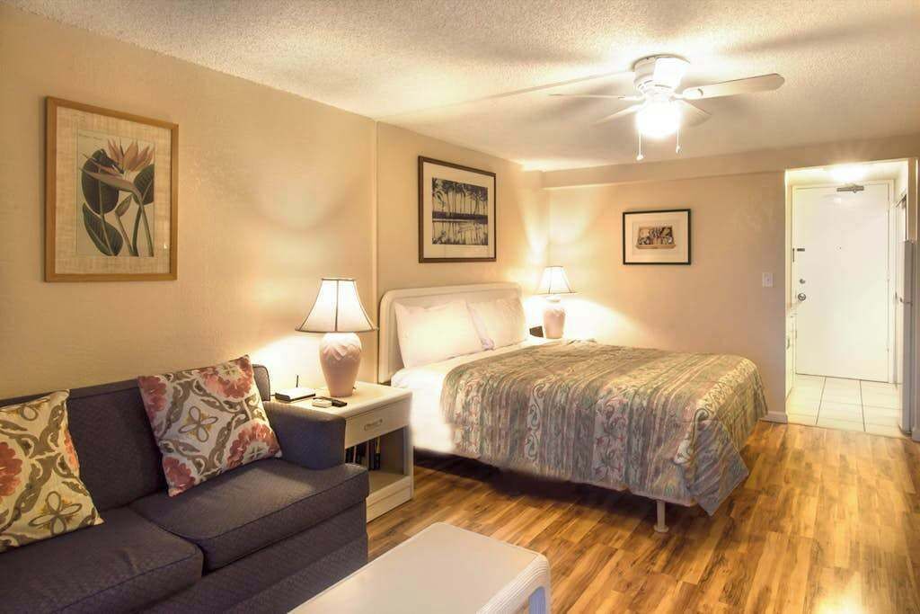 Une chambre à coucher avec un lit, une table de chevet, une lampe, un ventilateur de plafond et une porte.