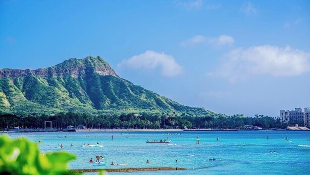A beach with clear blue water, a mountain in the background, and a few buildings along the shore. - *NEW* Diamond Head Cottage Near Waikiki, 30-Night Minimum (Honolulu)