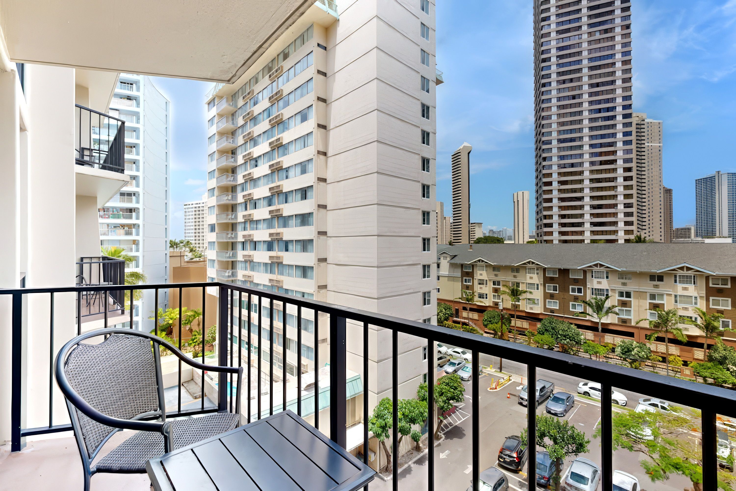 A balcony with a chair and table, overlooking a cityscape with high-rise buildings.
