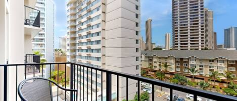 A balcony with a chair and table, overlooking a cityscape with high-rise buildings.