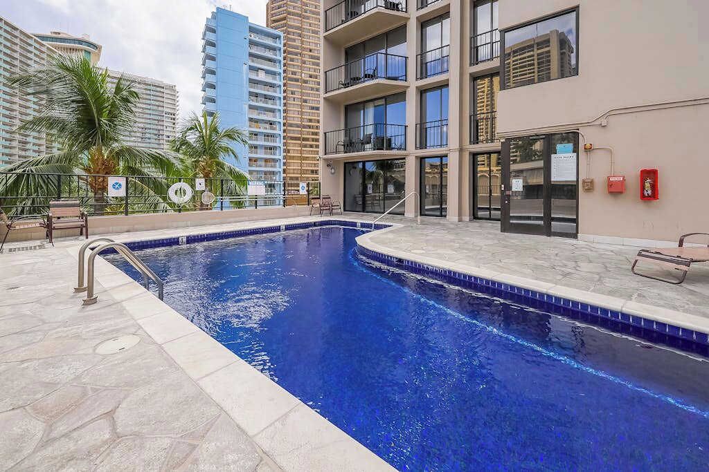 A swimming pool with a tiled edge, a metal handrail, and a palm tree in the background.