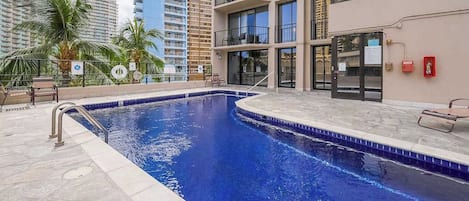 A swimming pool with a tiled edge, a metal handrail, and a palm tree in the background.
