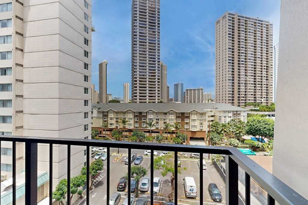 A high-rise building with a balcony overlooking a parking area and other buildings.