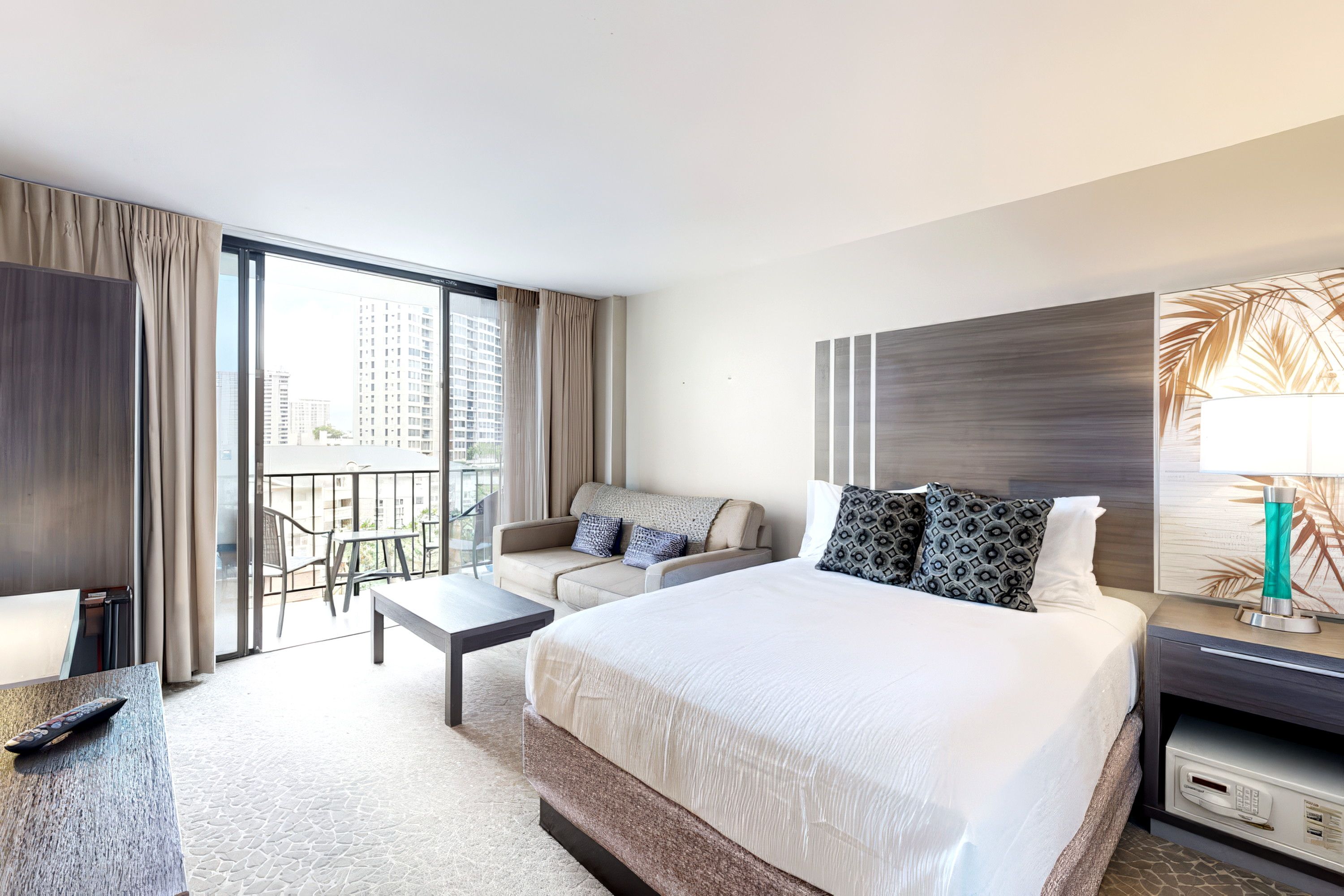 A hotel room with a large bed, a sofa, a desk, and a balcony with a view of the city.