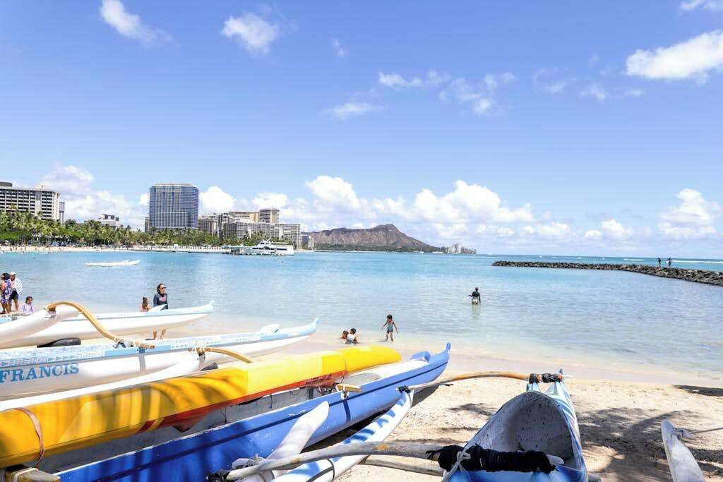 Ein Strand mit Kanus, blauem Himmel und Gebäuden im Hintergrund.