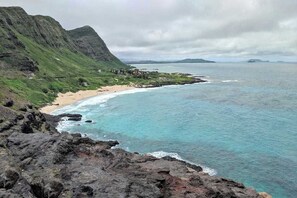 A coastal landscape with a beach, rocky terrain, and distant mountains.