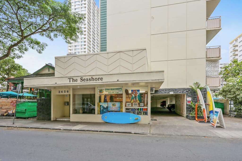 Ein Gebäude mit einem Schild, auf dem 'The Seashore' steht, und einem Surfbrett, das außen ausgestellt ist.