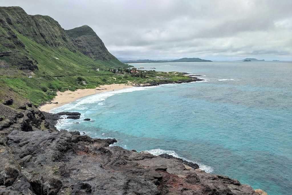 Un paisaje costero con una playa, terreno rocoso y montañas en la distancia.