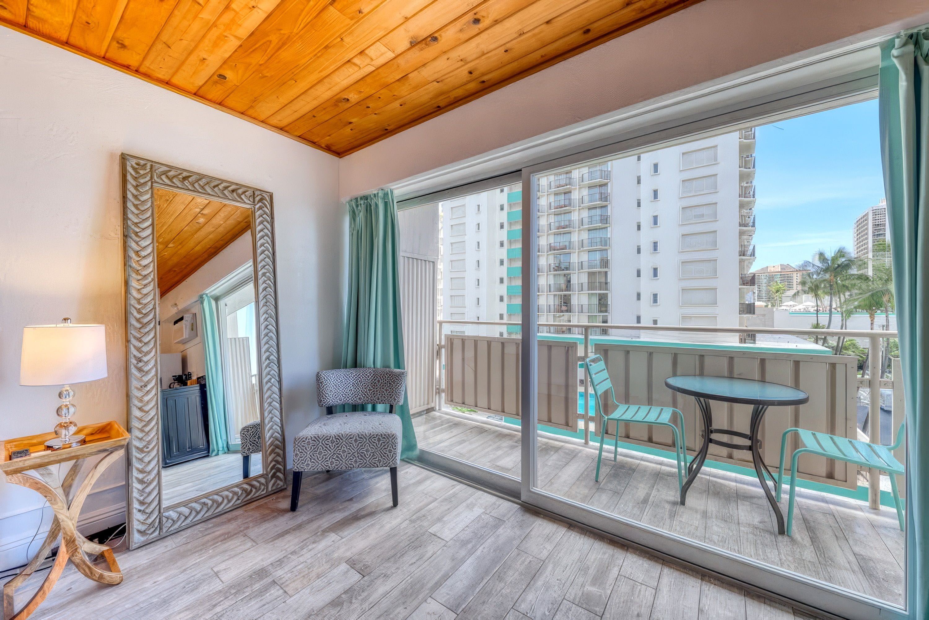 A balcony with a view of high-rise buildings, a chair, a table, and a large mirror.