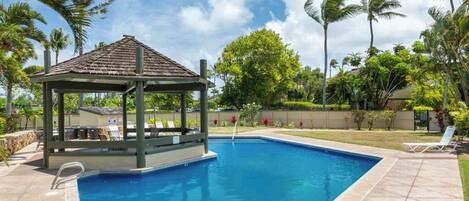 Una piscina con un pabellón, palmeras y cielo despejado.