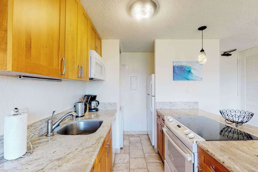 A compact kitchen with wooden cabinets, a microwave, a sink, a stove, and a ceiling light fixture.