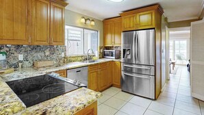 Una cocina con armarios de madera, un refrigerador de acero inoxidable, un microondas y una estufa negra.