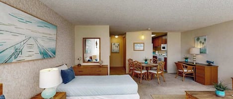 A hotel room with two beds, a desk, a dining area, and a kitchenette.