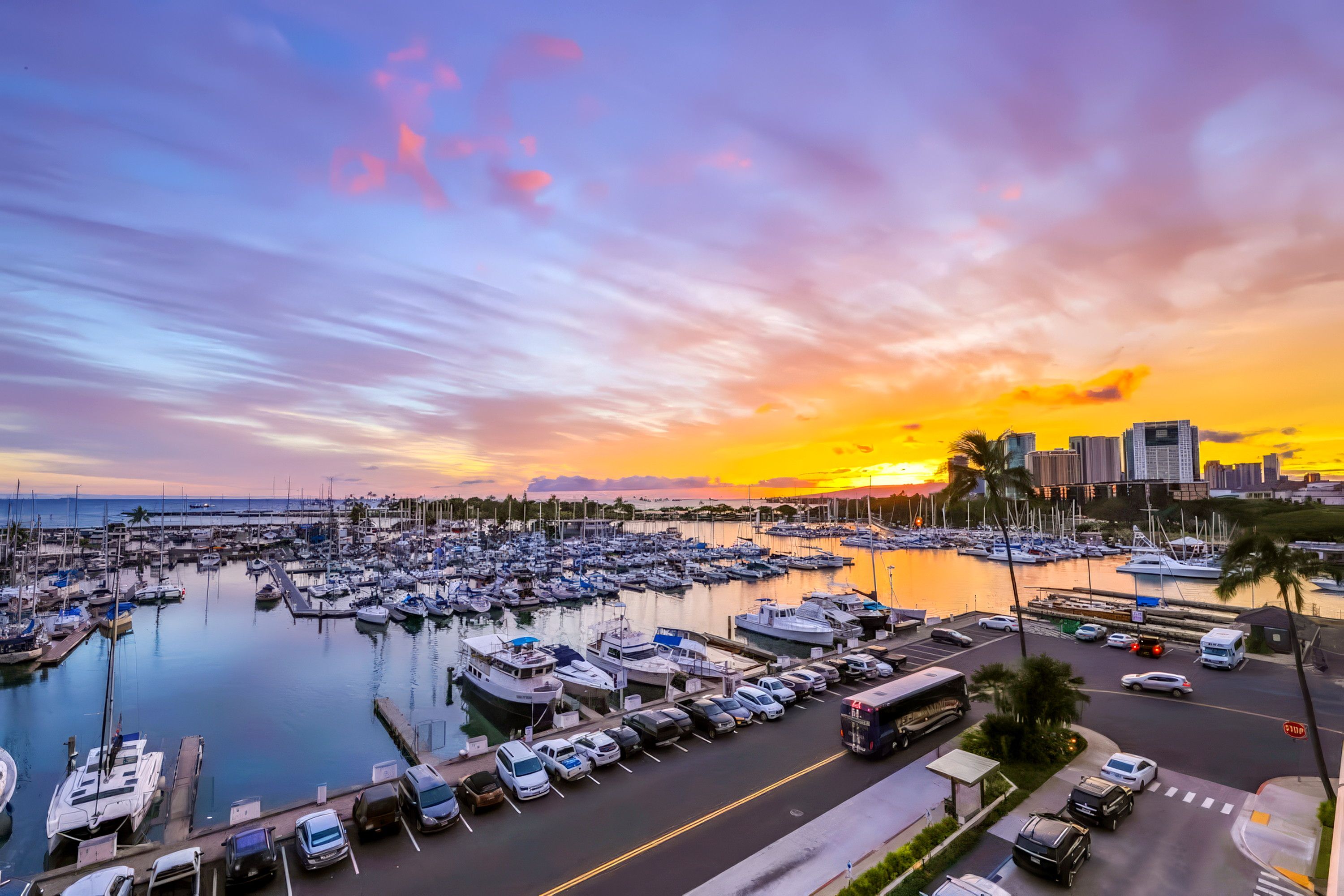 Un puerto deportivo con barcos amarrados, un horizonte urbano al fondo y una puesta de sol.