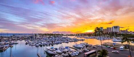 Un puerto deportivo con barcos amarrados, un horizonte urbano al fondo y una puesta de sol.