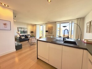 Eine moderne Küche mit Kochinsel, ein Essbereich mit einer Couch und Blick auf die Stadt.