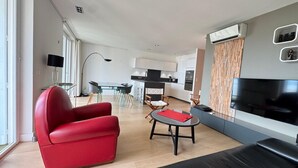 Uma sala de estar moderna com uma poltrona vermelha, uma mesa de jantar de vidro e uma televisão de tela plana.