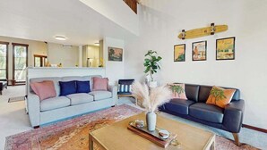 Un salón amplio con techo alto, una mesa baja de madera, dos sofás, una alfombra grande y una escalera.