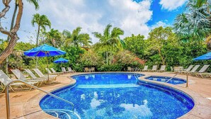 Una piscina con lettini e ombrelloni, circondata da palme e vegetazione tropicale.