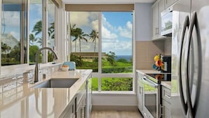 Une cuisine moderne dotée d’une grande fenêtre, d’appareils électroménagers en acier inoxydable et offrant une vue sur la verdure.
