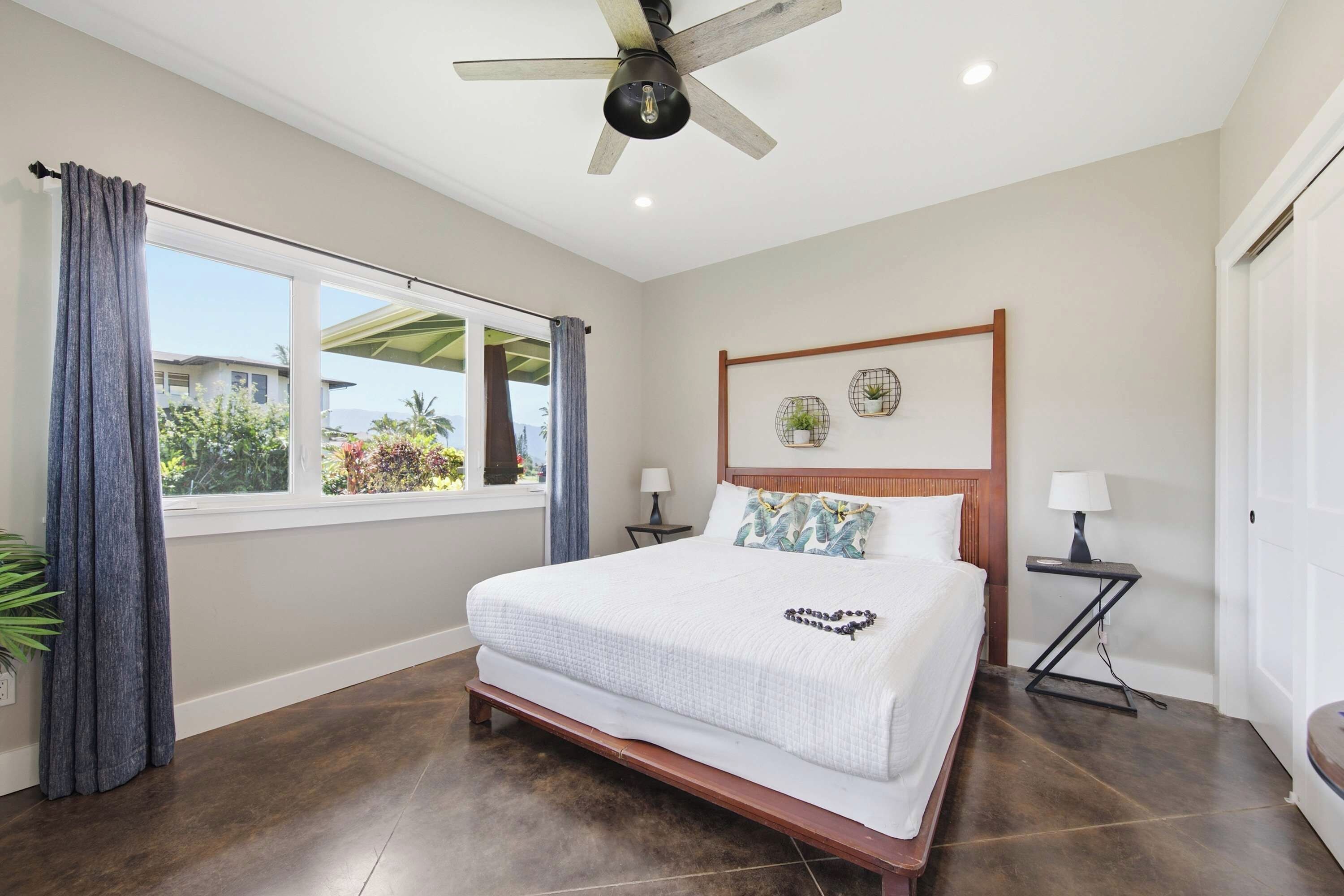 Un dormitorio con una cama grande, un ventilador de techo, una ventana con cortinas y vistas al exterior.
