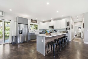 A modern kitchen with a central island, stainless steel appliances, and a bar area with stools. - The Palm House Family Retreat at Princeville - Mins to Beach, Shops, Dining (Princeville)