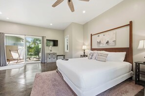 A bedroom with a large bed, a TV mounted on the wall, a ceiling fan, and a view of the outdoors through a sliding glass door. - The Palm House Family Retreat at Princeville - Mins to Beach, Shops, Dining (Princeville)