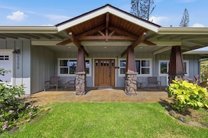 A two-story house with a stone foundation, a covered porch with wooden beams, and a front door with a window above it. - The Palm House Family Retreat at Princeville - Mins to Beach, Shops, Dining (Princeville)