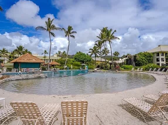 A pool area with lounge chairs, palm trees, and a building in the background.
