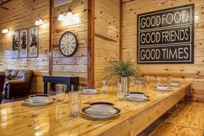 A wooden interior with a long dining table set for four, a clock, and a sign saying 'GOOD FOOD GOOD FRIENDS GOOD TIMES'. - Eat, Drink and Be Beary (Sevierville)