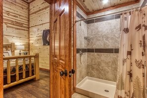 A wooden interior with a shower, a wooden door, and a small seating area with a bench and a lamp. - Eat, Drink and Be Beary (Sevierville)