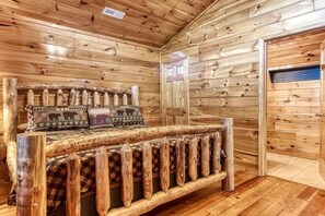Ein Holzhütten-Innenraum mit einem Bett, ausgestattet mit einer karierten Tagesdecke und Kissen mit Tiermotiven.
