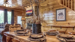 Un interior rústico de madera con una mesa de comedor preparada para cuatro personas, una araña y un letrero con motivos de osos.