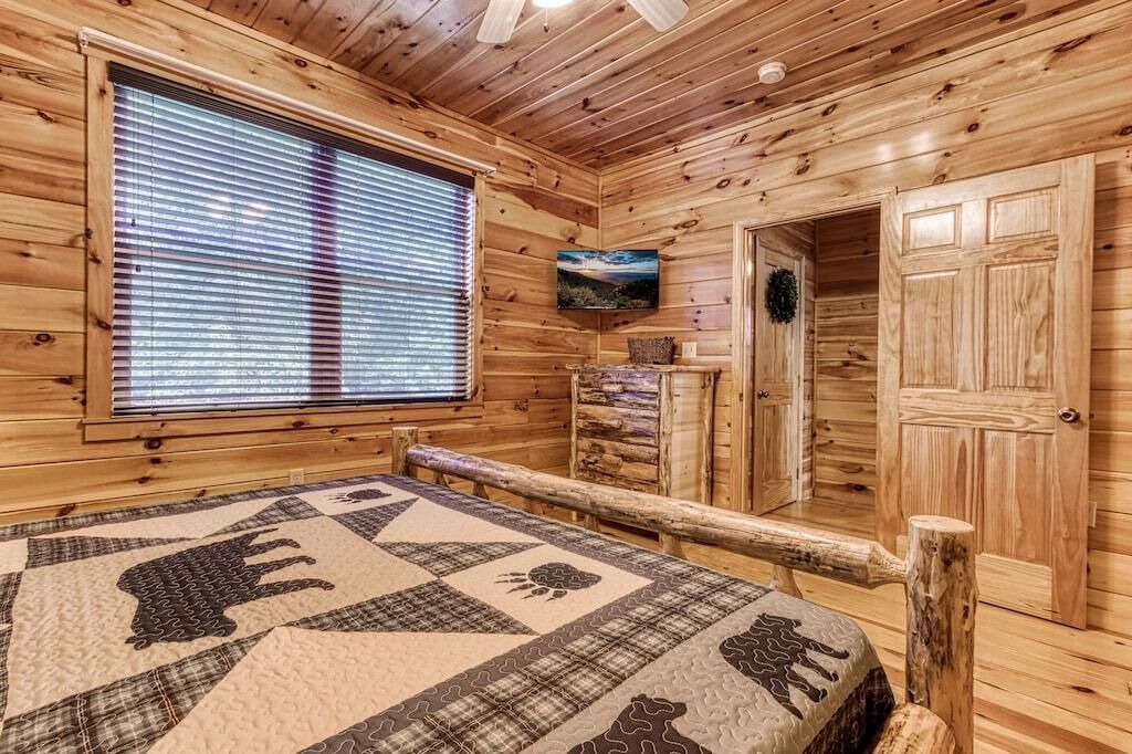 A log cabin room with a bed, a television, a fireplace, and a window with blinds.