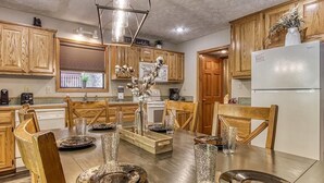 A kitchen with wooden cabinets, a dining table set for six, and a refrigerator. - Foxes Den (Pigeon Forge)
